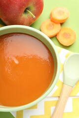 Baby food. Tasty puree in bowl and ingredients on green background, flat lay