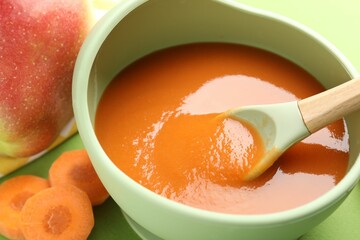Baby food. Tasty puree in bowl and ingredients on green background, closeup
