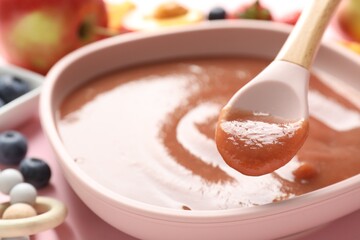 Baby food. Eating tasty puree with spoon at pink table, selective focus