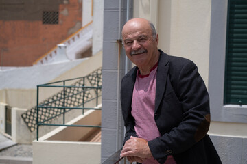 Fototapeta premium Elderly Spanish Man Walking in a Portuguese City and Looking at the Ocean. He Wears a Jacket and Has a Mustache