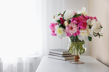Bouquet of beautiful peonies and books on white table indoors, space for text. Interior design