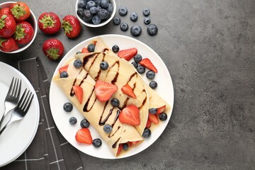 Tasty crepes with strawberries, blueberries and chocolate sauce on gray textured table, flat lay. Space for text