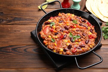 Tasty chili con carne in baking dish and flatbread on wooden table, closeup. Space for text