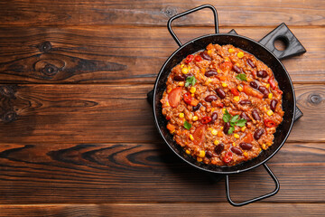 Tasty chili con carne in baking dish on wooden table, top view. Space for text