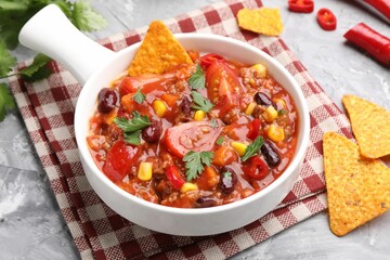 Tasty chili con carne in bowl and nachos on grey textured table, closeup