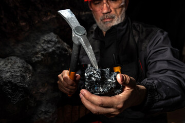 A man in a hard hat with a flashlight examines rock using a pickaxe. Geology, speleology, mining...