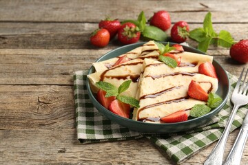 Tasty crepes with strawberries, chocolate sauce and mint on wooden table, closeup. Space for text