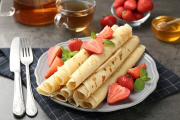 Tasty crepes with strawberries and mint on grey table, closeup