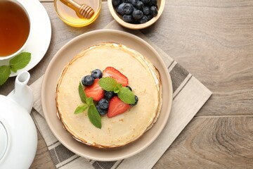 Delicious crepes with berries, cream, mint, honey and tea on wooden table, flat lay. Space for text