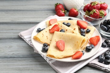 Delicious crepes with berries on grey wooden table, closeup. Space for text