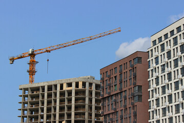 A tower crane over the frame of an unfinished building next to completed residential buildings
