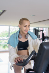 Non-binary gay man with mustache and androgynous appearance working out indoors in gym. Wearing...