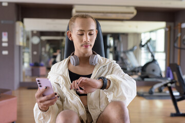 Non-binary gay man with mustache and androgynous appearance working out indoors in gym. Wearing feminine sports bra and using water bottle. Inclusive fitness concept with genderfluid representation.