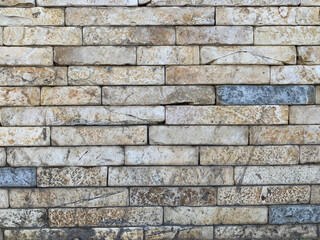 Wall of brick, fragment of old stone wall made of rectangular beige blocks with visible texture, stains, and natural cracks, weathered surface with earthy tones and rustic appearance