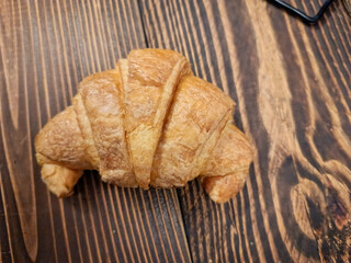 A flaky croissant rests on a dark wooden table.