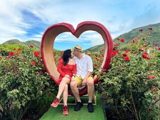Romantic couple sitting inside heart sculpture in flower garden, summer love, travelling