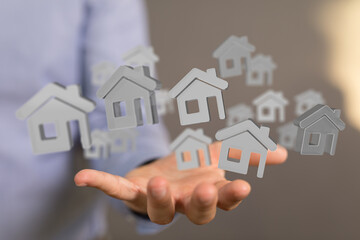 Image of a real estate agent's hand holding multiple digital house icons, representing property listings or the housing market.