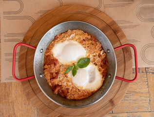 shakshuka in a round pan stands on a table in a street cafe, top view