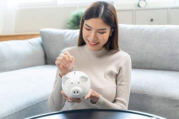 Young woman saving money monthly expenses putting coin in to piggy bank on the table.