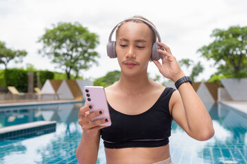 Genderfluid gay man with mustache and lipstick relaxing poolside while wearing a bikini-style top....