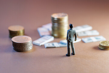 Businessman figurine contemplating financial success with stacks of coins and bills in a minimalist...