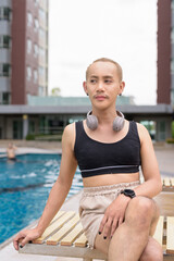 Genderfluid individual with mustache and lipstick relaxing poolside while wearing a bikini-style...