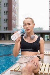 Genderfluid individual with mustache and lipstick relaxing poolside while wearing a bikini-style...