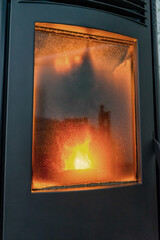 Vertical shot of a modern pellet stove in full operation with a large flame and a very dirty door window. Renewable and sustainable energy, ecological heat.