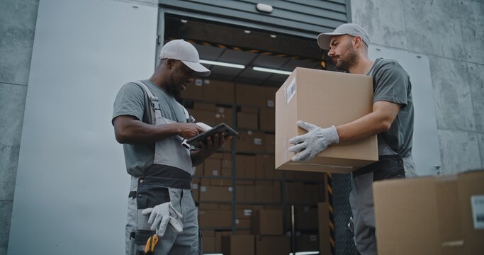 Diverse Workers Taking Cardboard Boxes with Online Orders and E-Commerce Goods to Logistics Retail Warehouse. African American Manager Scanning Parcels with Barcode Scanner, Using Tablet Computer.