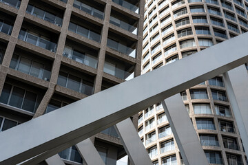 Intertwining vertical and diagonal architectural elements create a dramatic composition of urban surfaces, sharp lines and contrasting textures under intense daylight in a contemporary city setting.