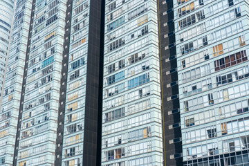 Modern high-rise facade featuring repeating geometric window grids and subtle color variations, evoking an abstract rhythm and contemporary urban surfaces under bright daylight in a vibrant cityscape.