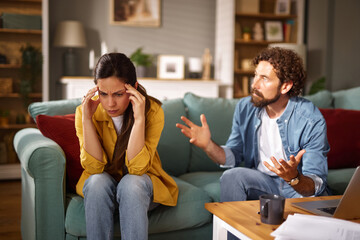A woman appears stressed, holding her head while a man gestures passionately about their financial...
