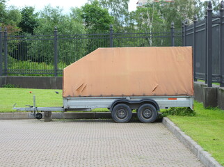 A four-wheeled awning car trailer stands against a lattice fence, Iskrovsky Prospekt, St. Petersburg, Russia, June 26, 2025
