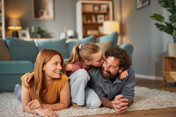 A playful family spends quality time in their cozy living room, with a young girl kissing her...