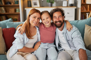 A joyful family spends quality time together on the sofa at home, with a young girl nestled between...