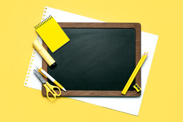 Top view of black school chalkboard with wooden frame with space for text on a white sheet of paper and school supplies. Back to school concept