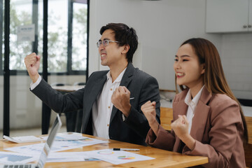 Celebrating Success: Two business professionals, a man and a woman, express their excitement and success with raised fists, showcasing teamwork and achievement in a modern office setting.