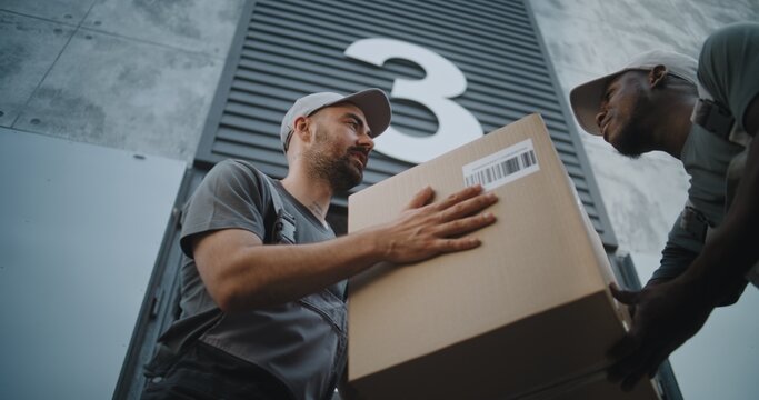 Outside of Logistics Retail Warehouse: Employee Taking Cardboard Box with Online Orders and E-Commerce Goods from African American Worker of Express Delivery Service. Low Angle Shot. Slow Motion.