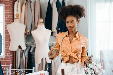 A woman tailor in an orange shirt is standing in front of a mannequin. She is holding a measuring tape and measuring the dress. She is a tailor in a clothing store.