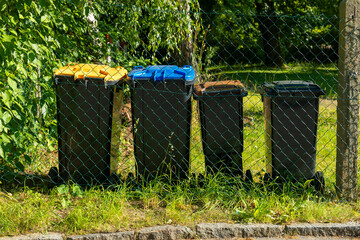 Colorful recycling bins lined up against a green backdrop on a sunny day in a residential...