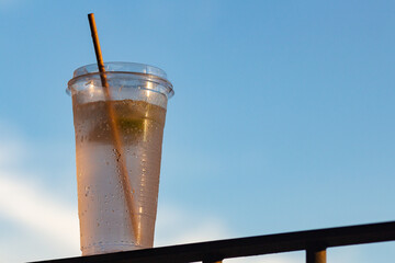A plastic cup holding a cool beverage against a bright blue summer sky - emphasizing thirst for...