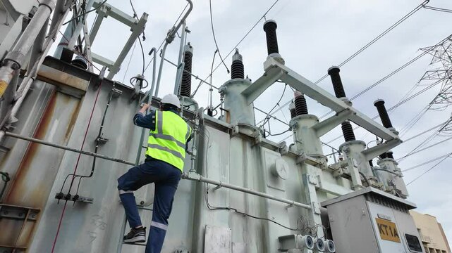 Worker inspects power transformer and control cabinet at outdoor electrical substation with industrial equipment ensuring safety and proper operation under cloudy sky maintenance control