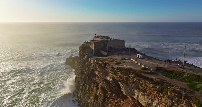 Aerial view of the lighthouse located on a huge cliff and offering a view of the huge ocean waves of Nazare, Portugal