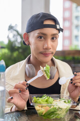 Young non binary gay man eating salad