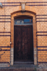 Rustic wooden door framed by textured orange and yellow brickwork in a quiet urban setting during midday