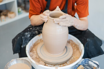 Close-up of a potter's hands making a ceramic vase on a potter's wheel. 