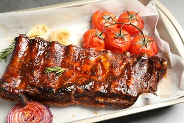 Delicious spare ribs, rosemary, baked onion and sun dried tomatoes on grey table, closeup
