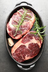 Pieces of raw beef meat and spices in baking dish on gray textured table, top view