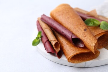 Delicious fruit leather rolls and mint on light table, closeup. Space for text