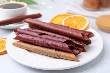 Tasty fruit leather rolls and orange slices on white table, closeup